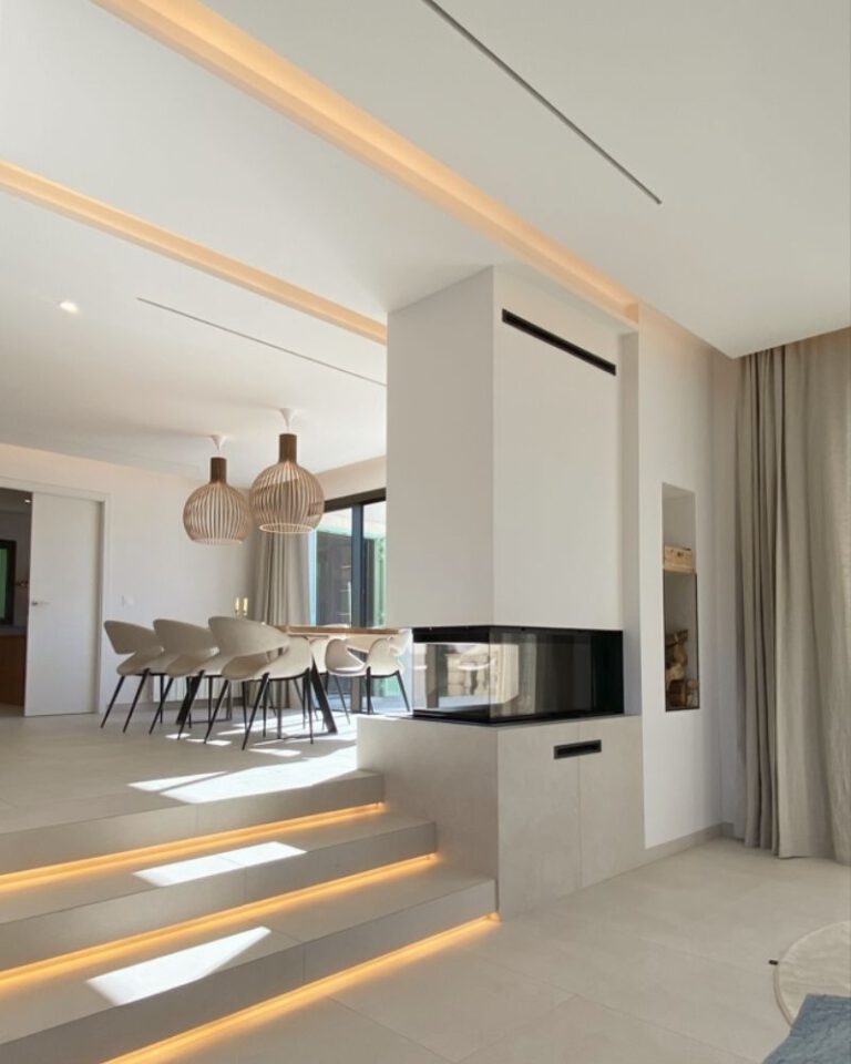 Salón-comedor minimalista de una reforma en Marratxí (Palma) con chimenea central y escalones con luz LED