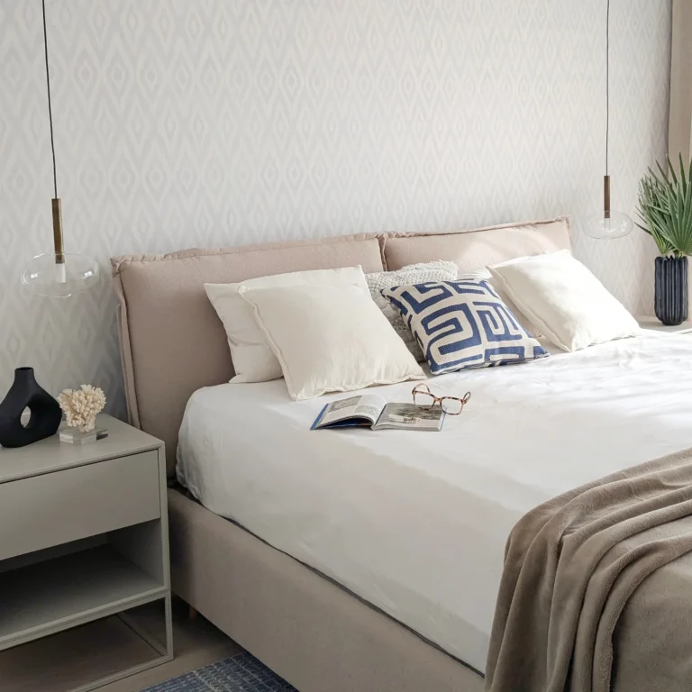 Dormitorio en tonos beige con cabecero tapizado, cojines estampados y mesitas suspendidas
