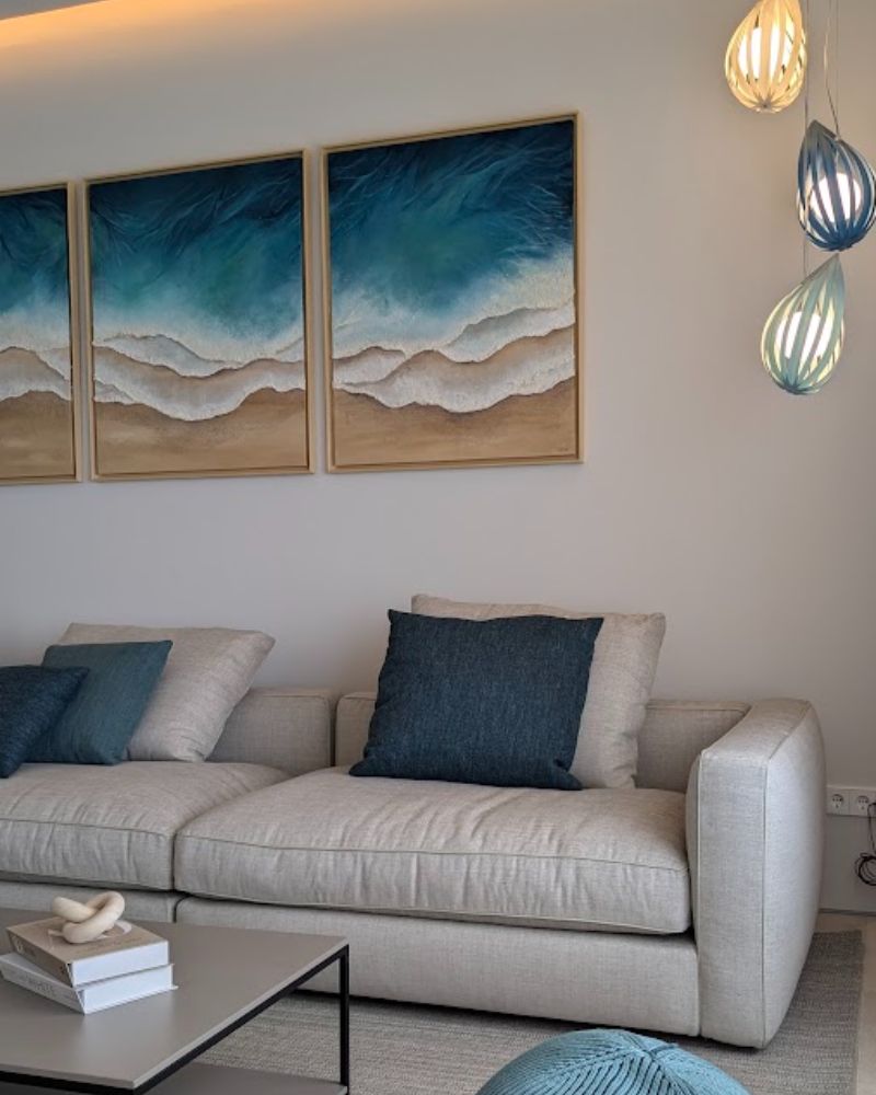 Salón con sofá beige, cojines azules y tríptico marino en un proyecto de interiorismo en Port d'Andratx, Mallorca