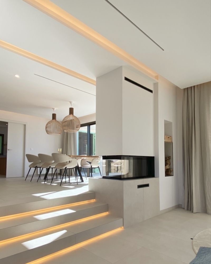 Salón comedor de diseño con chimenea y luz LED indirecta en una reforma en Marratxí, Mallorca