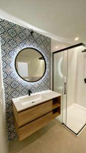Baño reformado con baldosa hidráulica azul, espejo redondo y mueble de roble, reforma integral en Mallorca