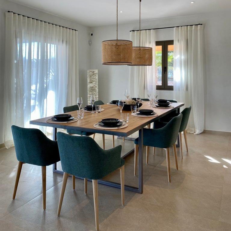 Comedor con mesa de madera y sillas tapizadas en verde en una vivienda de Campos, Mallorca