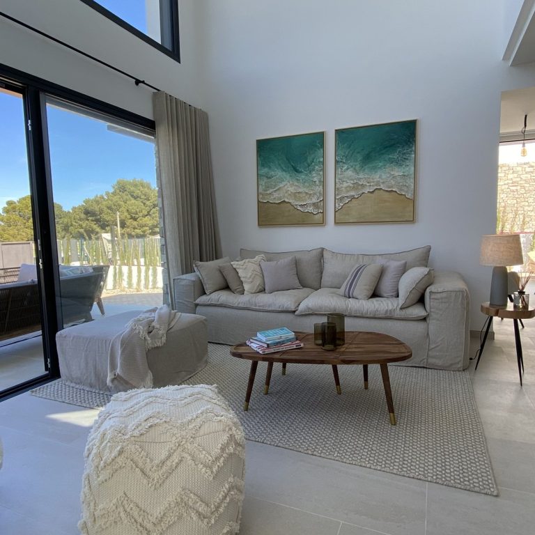 Salón de doble altura con sofá beige y salida a la terraza en una casa de Mallorca