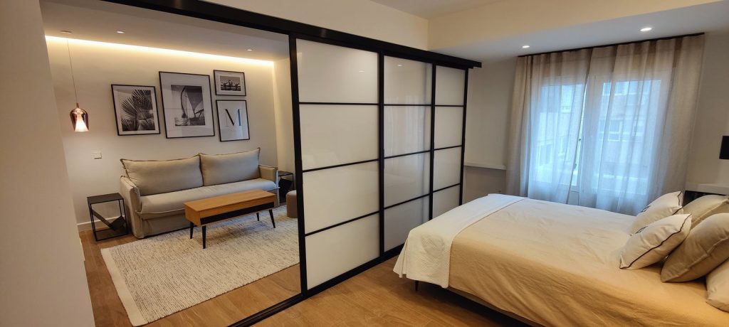 Salón con sofá beige y láminas náuticas en piso reformado de Madrid, tras la corredera de cristal abierta