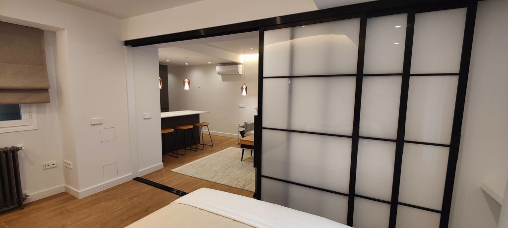 Cocina abierta con barra y taburetes vista desde el dormitorio en piso reformado de Madrid