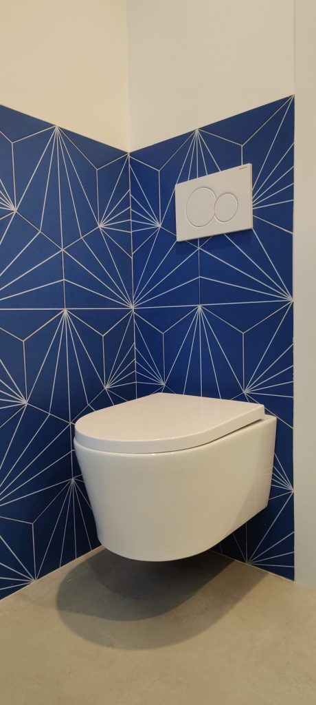 Aseo con pared de azulejo geometrico azul en el piso reformado de Madrid