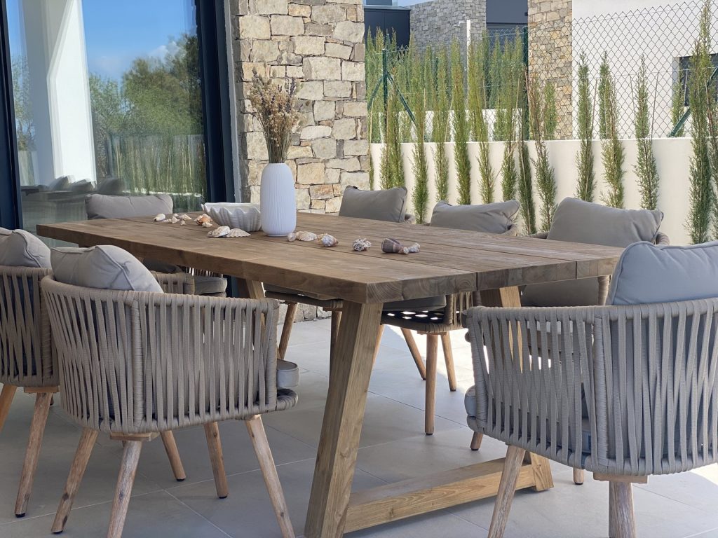 Comedor exterior en Colònia de Sant Pere, Mallorca, con mesa de madera maciza, sillas de cuerda y conchas marinas