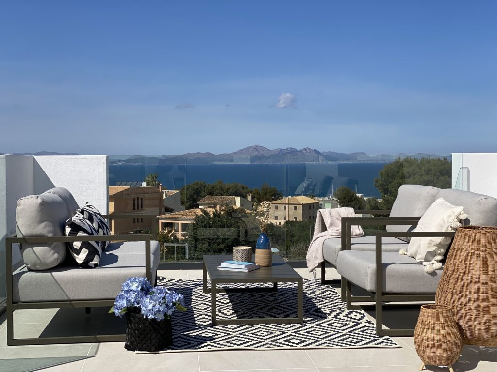 Terraza superior en Colònia de Sant Pere, Mallorca, con sofás grises, alfombra de rombos y vistas a la bahía