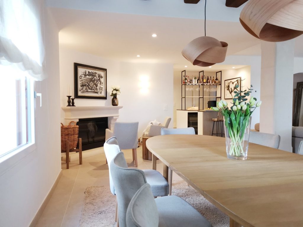 Comedor reformado en Santa Ponsa, Mallorca, con chimenea de piedra, mesa oval de madera y zona de bar