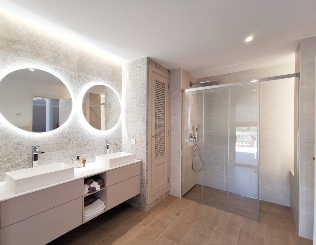 Baño reformado en Santa Ponsa, Mallorca, con doble lavabo, espejos retroiluminados y gran ducha de cristal