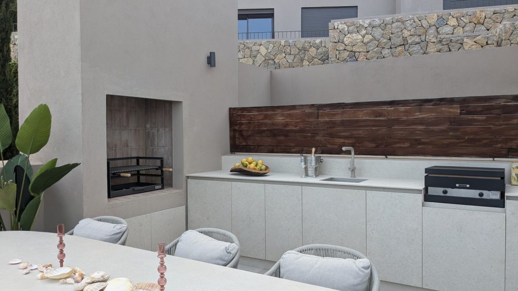 Cocina exterior en villa de Puerto Andratx, Mallorca, con barbacoa de obra, encimera clara y friso de madera