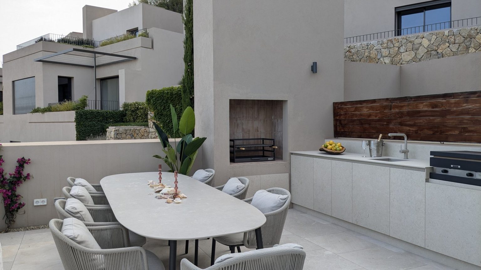 Terraza con comedor exterior en Amber Village, Puerto Andratx: mesa oval, sillas de cuerda y barbacoa de obra