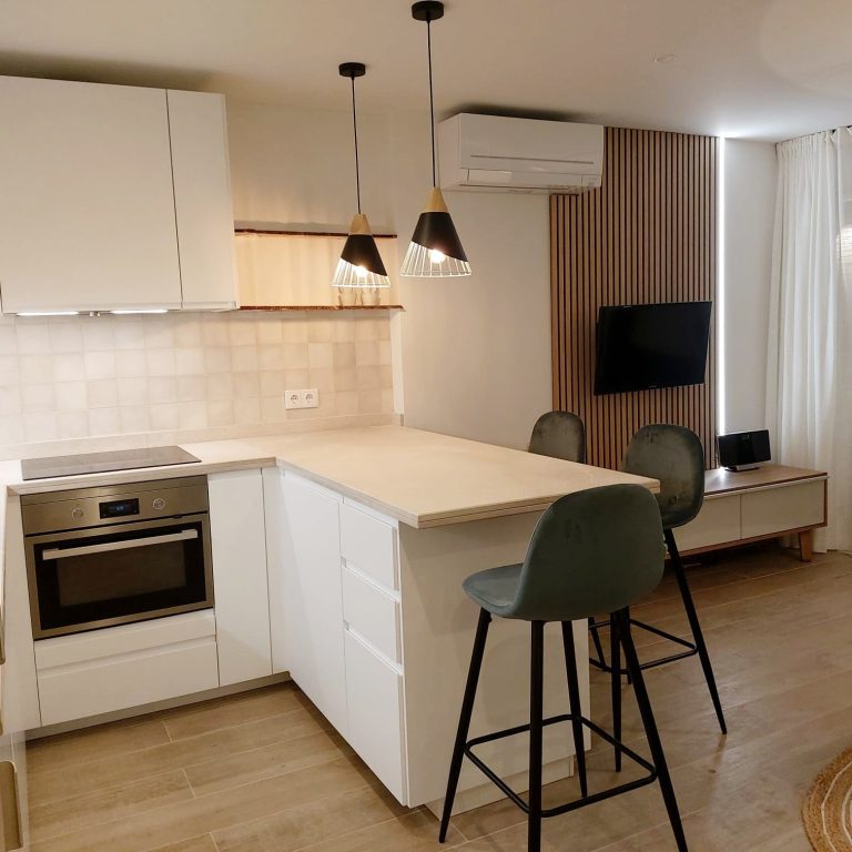 Cocina blanca abierta con barra y taburetes verdes en un apartamento de Magaluf, Mallorca