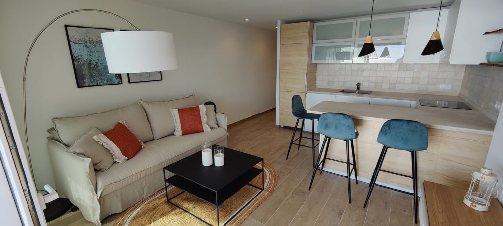Salón con sofá beige y barra de cocina con taburetes azules en un apartamento de Magaluf, Mallorca