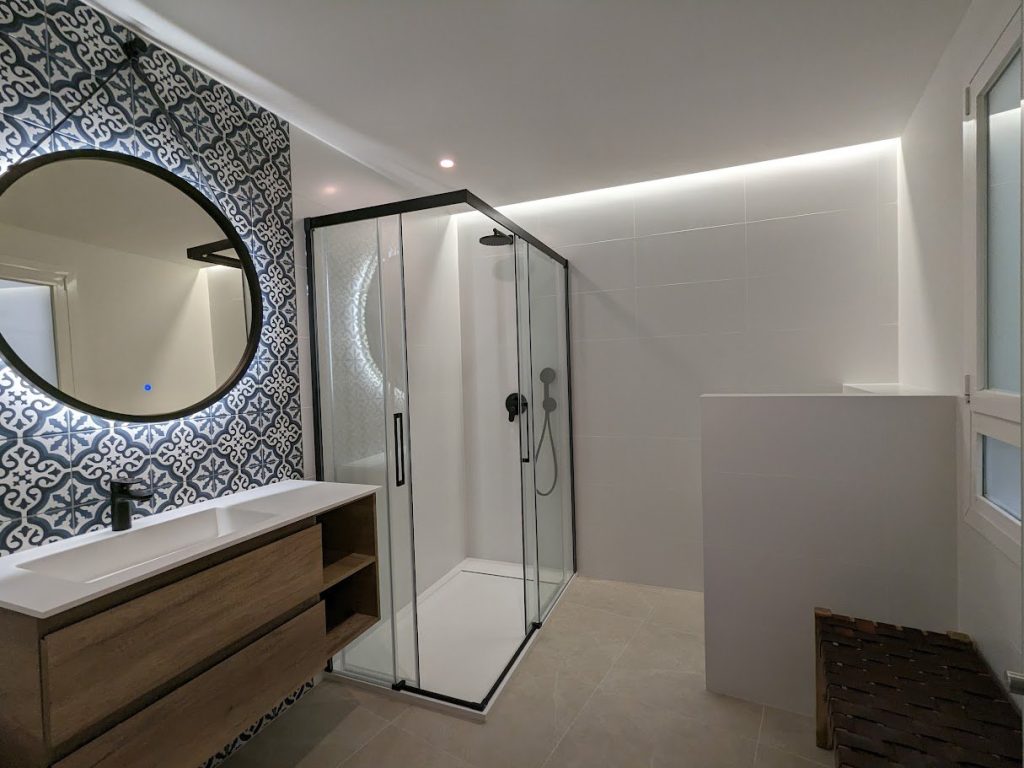 Baño con pared de baldosa estampada en azul y espejo redondo en Palma de Mallorca