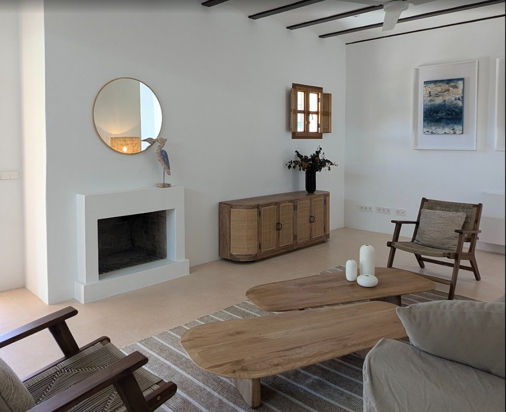 Salón de estilo payés con chimenea blanca y muebles de madera natural en una casa de Ibiza