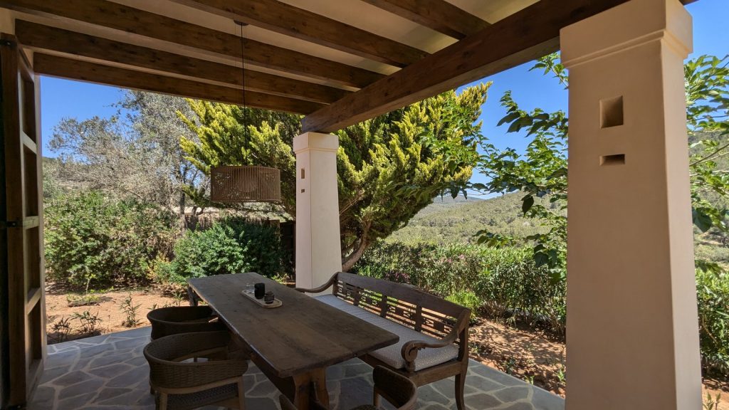 Porche con vigas de madera y comedor exterior con vistas al campo en una finca de Ibiza