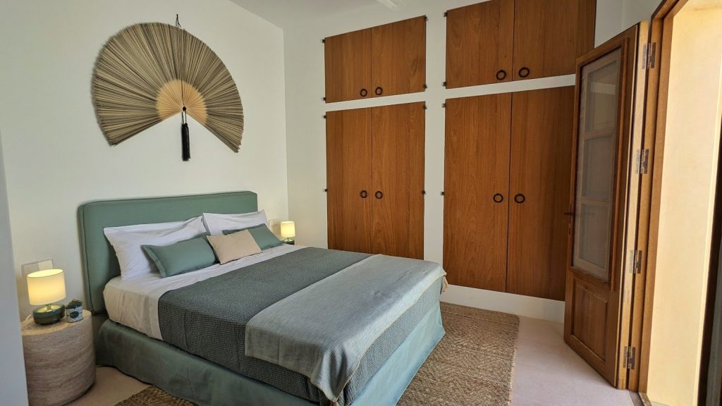Dormitorio con cama verde salvia y armarios de madera en una casa de Ibiza