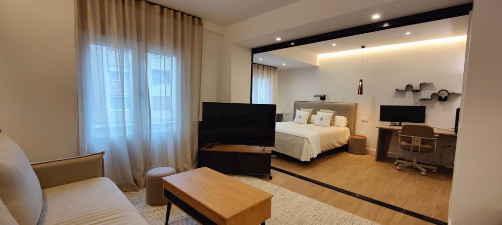Dormitorio reformado en Madrid con televisor, escritorio y cama frente a la zona de estar