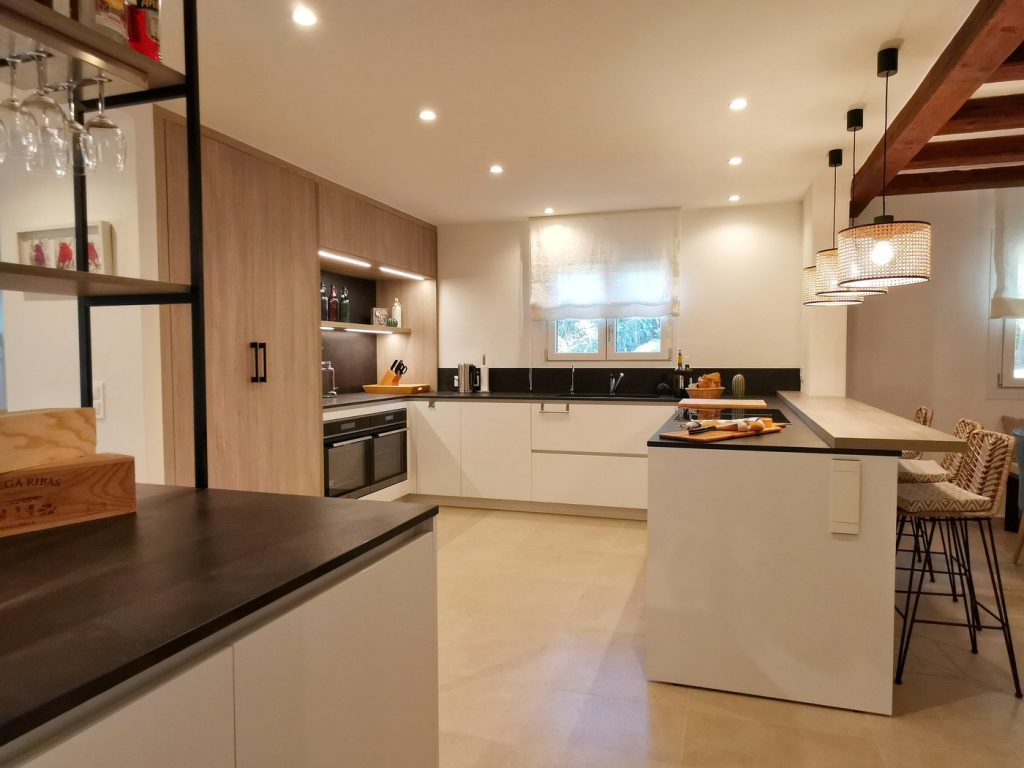 Cocina reformada en Santa Ponsa, Mallorca, con muebles blancos y madera, encimera oscura y barra con taburetes