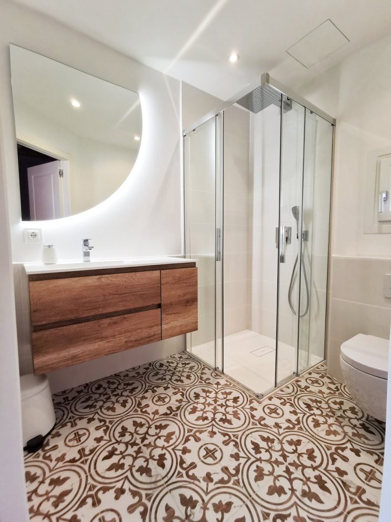 Baño reformado en Santa Ponsa, Mallorca, con suelo hidráulico, mueble de madera y ducha esquinera de cristal