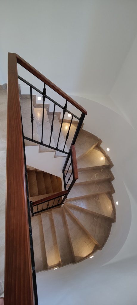 Escalera curva de mármol tras la reforma en Santa Ponsa, Mallorca, con barandilla de forja y madera