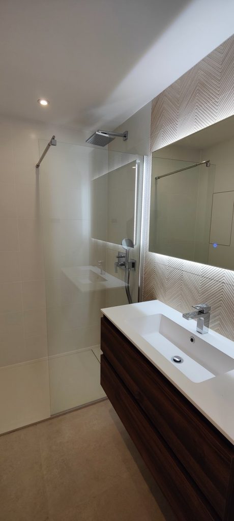 Baño con ducha de vidrio, azulejo en espiga y mueble de madera oscura en Magaluf, Mallorca