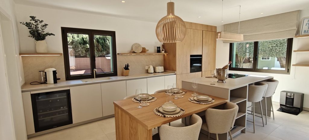 Cocina reformada con mesa de madera integrada, isla y vinoteca en Marratxí, Mallorca