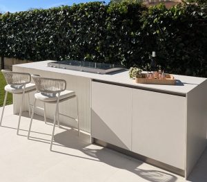 Cocina exterior con barra de porcelánico y taburetes junto a un seto, proyecto en Marratxí
